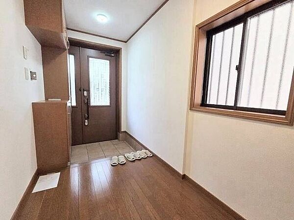 ガラス窓付きの玄関ドアと小窓から自然光が入る明るい玄関スペースです。落ち着いた木目調のフロアと建具が調和し、住まいの顔として温かみのある空間を作り出しています。
