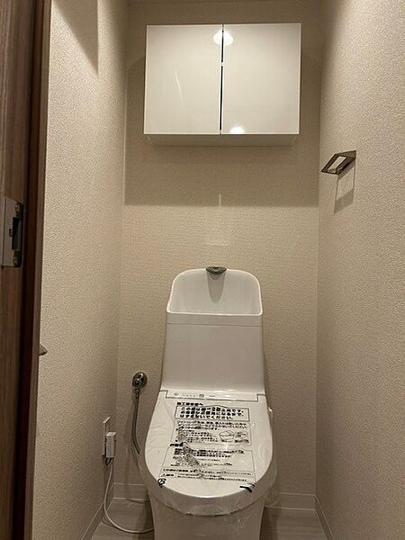 白で統一された清潔感あふれるレストルーム！トイレットペーパー等のストックをすっきり隠せる便利な上部吊戸棚を完備。やさしい色合いの壁紙と手洗いしやすい深型ボウルで、快適に使える空間です。