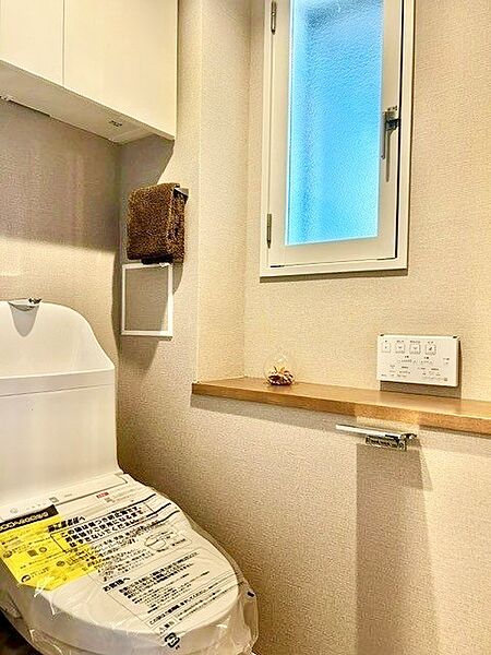 換気や採光に優れた小窓と、小物を飾れるカウンターを備えた爽やかなトイレ空間！新品の一体型温水洗浄便座や上部吊戸棚、壁掛けリモコンを完備。シックなグレージュクロスが上質な寛ぎを演出します。