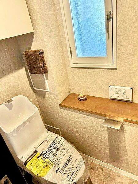自然光を取り込める小窓と、小物を飾れる木目カウンターを備えた爽やかなトイレ！新品の一体型温水洗浄便座や壁掛けリモコン、上部隠せる吊戸棚を完備。シックなグレージュクロスが寛ぎを演出する快適空間です。