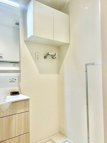 上部に扉付きの吊戸棚を備えた機能的な洗濯機置場！洗剤や生活用品をスッキリ収納でき、空間をきれいに保てます。洗面化粧台のすぐ横に配置され、水回りの家事動線もスムーズな快適設計です。