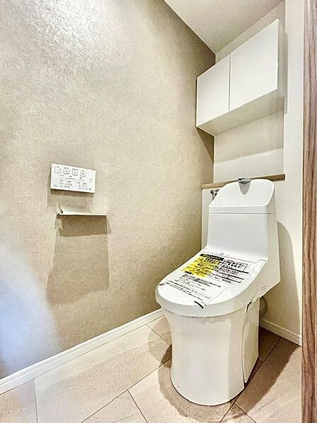 ニュアンスのある壁紙が落ち着いた雰囲気を演出するトイレ!手洗い一体型の温水洗浄便座を採用しています。上部には扉付きの吊戸棚を備えており、ストック類をすっきり隠して収納できる機能的な空間です。