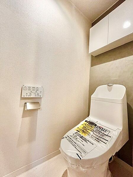 手洗い一体型で清潔感のある温水洗浄便座付きトイレ！上部にはトイレットペーパーや掃除用品を隠して収納できる便利な吊戸棚を設置。シックなアクセントクロスがおしゃれで落ち着く快適な個室空間です。