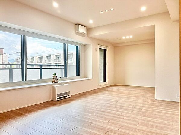 ワイドな大きな窓から豊かな自然光が広がる開放的なリビング！明るい木目調フローリングとダウンライトが温もりある空間を演出します。奥行きがあり、陽光を感じながらゆったり過ごせる心地よい居室です。