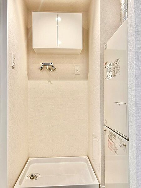 洗濯機置場の上部に便利な吊戸棚を備えた清潔感あふれるスペース！洗剤やランドリー用品をすっきり収納できます。右手にはボイラー等の設備がコンパクトに収まり、限られた空間を有効活用した機能的な設計です。