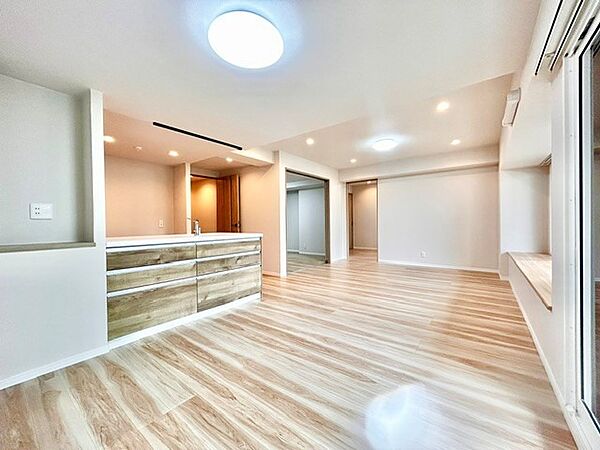 ナチュラルテイストの統一感が魅力的な大空間リビング！対面キッチンから部屋全体を見渡せ、奥の洋室へもスムーズに移動できる生活動線が優れています。ダウンライトの優しい光が空間を上品に演出します。