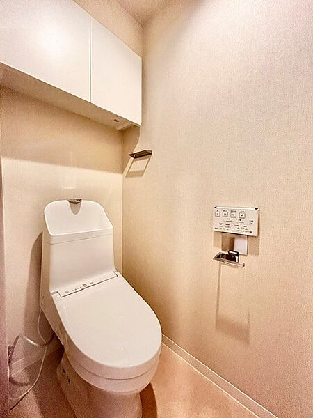 白を基調とした清潔感あふれる温水洗浄便座付きトイレ！上部にはトイレットペーパーや備品をしっかり収納できる棚を備えており、生活感を隠してすっきり保てます。スタイリッシュで快適な空間です。