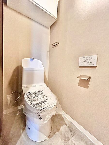 温水洗浄便座付きの清潔感あふれるトイレ！トイレットペーパーや掃除用品をすっきり収納できる吊戸棚を完備。壁付けのリモコンやスタイリッシュなペーパーホルダーを備えた快適なプライベート空間です。