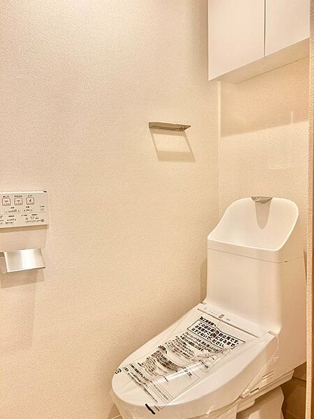 白を基調とした清潔感あふれる快適トイレ！手洗い一体型の温水洗浄便座を採用し、上部にはトイレットペーパーなどをすっきり隠せる吊戸棚を備えています。壁付けリモコンも完備した機能的なレストルームです。