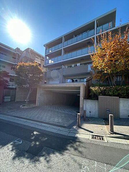 陽光あふれるエントランス。明るい日差しが、建物の洗練された外観と植栽を優しく照らします。