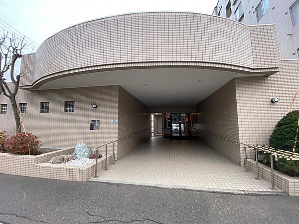 曲線を描くタイル張りの外観が印象的なエントランス。屋根のあるアプローチには手すりが付き、奥へと続きます。植栽が彩りを添える落ち着いた佇まい。ベビーカーや荷物持参の際の通りやすさを現地で確かめられます。