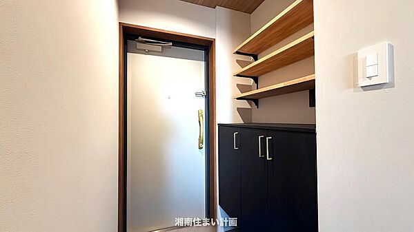 空間を引き締めるモダンなブラックのシューズボックスと木のぬくもりが感じられるオープンシェルフを設置。クローズド収納で生活感を抑えつつ、可動棚は魅せる収納として、意匠性と実用性を両立させました。