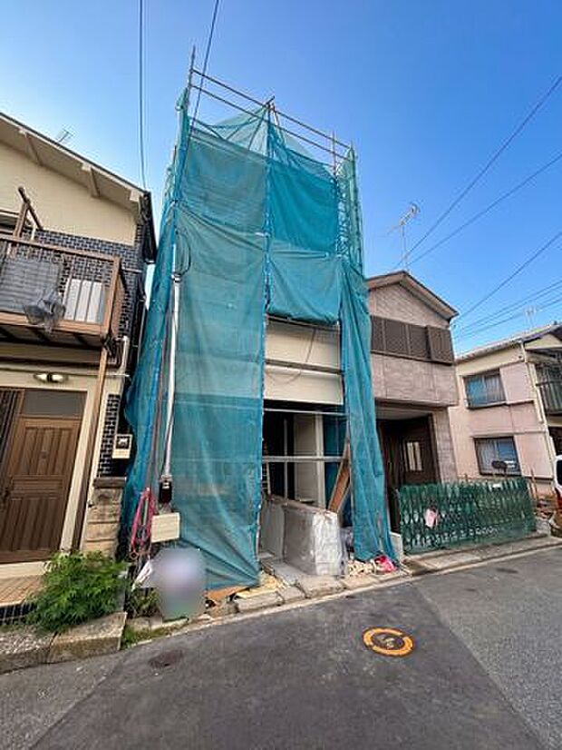 建築中の建物を正面から確認できる現地写真。前面道路との位置関係や周辺の住宅街の様子も分かりやすく、建物の完成後をイメージしながら現地の雰囲気を確認できる一枚です。