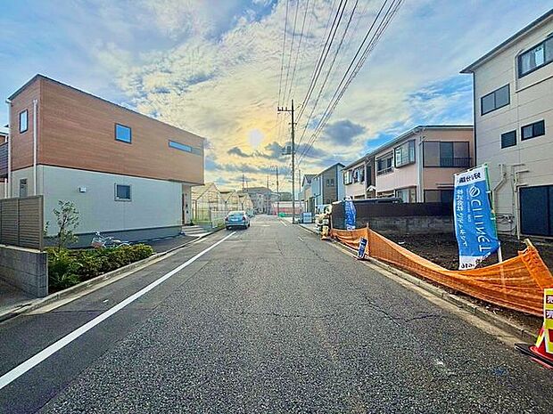 住宅街の道路沿いに位置する住まいで、周辺には戸建住宅が並んでいます。前面道路の様子や周囲の街並みを確認でき、現地の雰囲気が伝わる写真です。