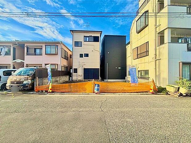前面道路と建物を一緒に捉えた外観写真。建物全体の雰囲気に加え、敷地前の道路や周辺の住宅も確認でき、現地の街並みや住まいの立地環境が伝わる一枚です。