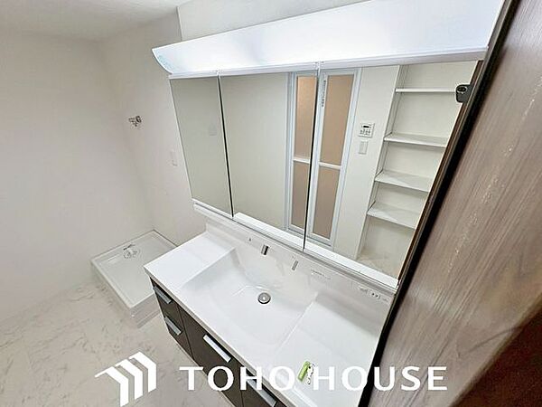 大型の鏡（または三面鏡仕様）を備えた、機能的なシステム洗面化粧台。身支度がしやすい広い洗面ボウルや、散らかりがちな洗面小物をスッキリと隠して片付けられる充実の収納スペースが完備されています。