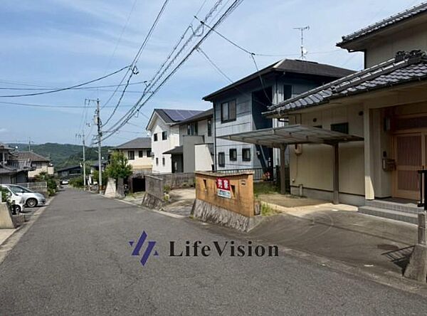 ベージュ外壁と瓦屋根が街並みに馴染む外観。前面道路6mで駐車も快適。木目の玄関が温かみを添え、落ち着いた住宅地の雰囲気が感じられる一邸です。