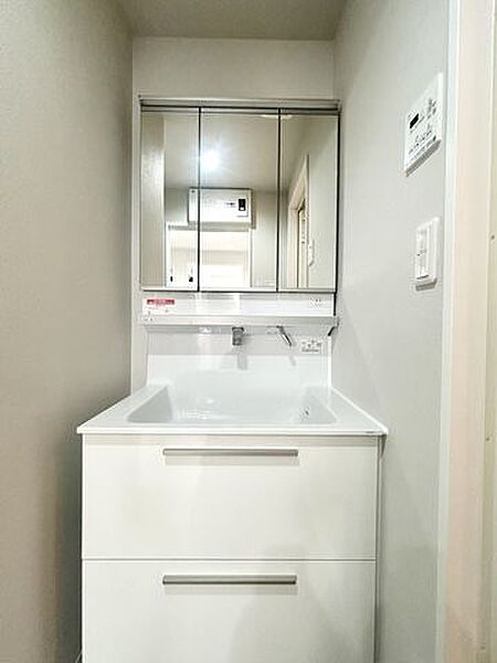 【洗面】三面鏡と明るい照明を備えた、シンプルで清潔感のある洗面化粧台です。