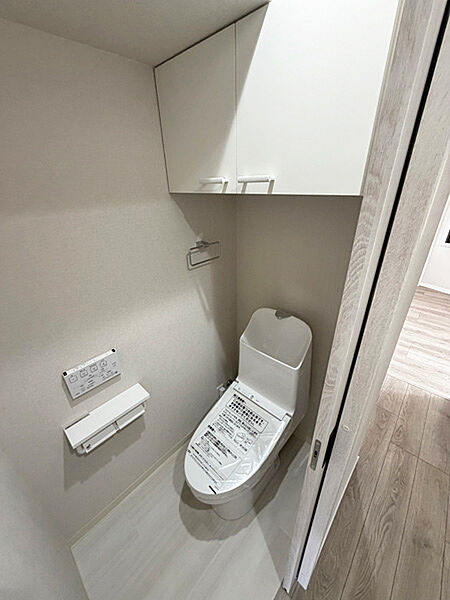 温水洗浄便座付きのトイレ。 上部に収納棚を備え、トイレットペーパーや清掃用品をすっきり収納