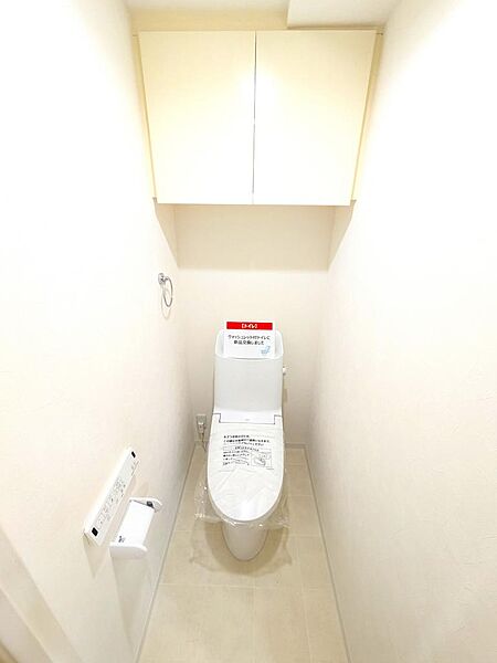 【トイレ】上部にはトイレットペーパーや掃除用品などをすっきりと目隠し収納できる吊戸棚を完備。限られた空間を有効に活用できる嬉しい設計です。床や壁面も明るいトーンでまとめられ、清潔感があります。