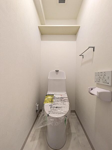 洗浄機能付きのトイレ。トイレットペーパーのストックを置ける棚もあります。汚れが分かりやすい白の床やクロスは、清潔な状態を保ちやすいです。