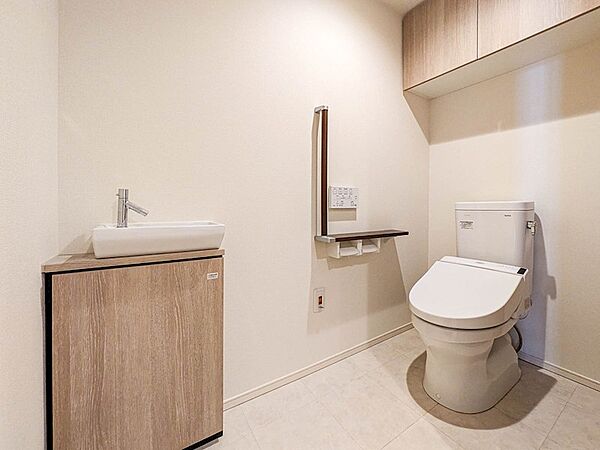 車椅子での利用や介助にも配慮し、スペースが確保された広めのトイレ。手すりや独立した手洗い器付き。