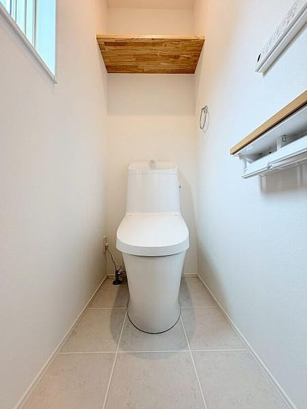 トイレはシンプルなデザインで清潔感のある空間です。窓があり自然な明るさが感じられます。壁の上部に棚が設けられているため収納にも便利です。床はお手入れがしやすい素材を採用しています。