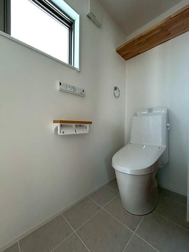 シンプルなデザインのトイレで清潔感のある空間です。窓から自然光が差し込み明るさを感じられます。収納スペースも備わっており使い勝手に配慮されています。壁や床の色合いも落ち着いています。