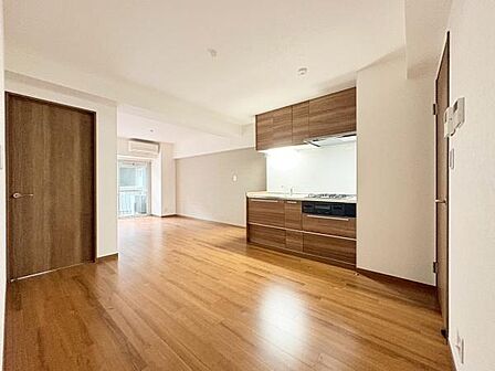 木目調のフローリングとキッチン収納が空間に統一感を与えています。扉や建具も同じトーンで揃えられ全体的に落ち着いた印象です。窓からの採光で室内は明るく開放感があります。