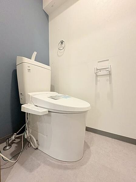 シンプルなデザインのトイレです。清潔感のある空間が広がっています。壁紙と床材のコントラストが特徴的です。ゆとりあるスペースで快適にご利用いただけます。温水洗浄便座も設置されています。