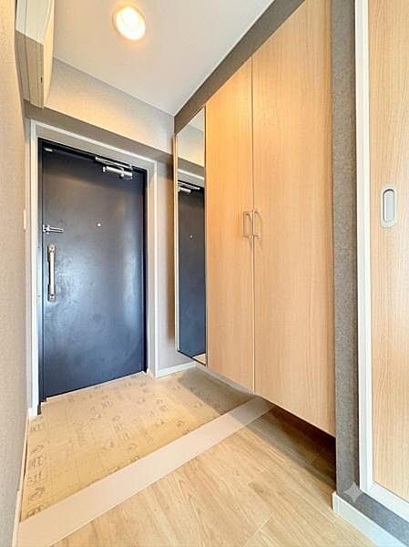 玄関は明るい雰囲気でミラー付きの収納が備わっています。木目調の扉が温かみを演出します。出入口付近はスペースが確保されていて日々の出入りもスムーズです。フロアや壁も落ち着いた色合いでまとめられています。