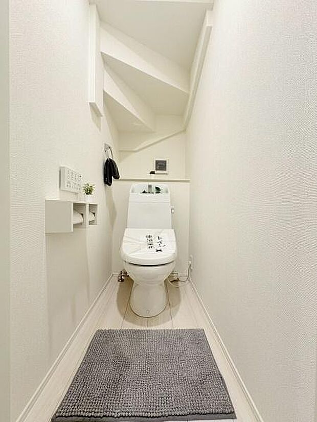 全体が白を基調とした清潔感のあるトイレです。壁面収納や棚がすっきりと設置されておりスペースを有効活用しています。照明が明るく天井のデザインも特徴的です。