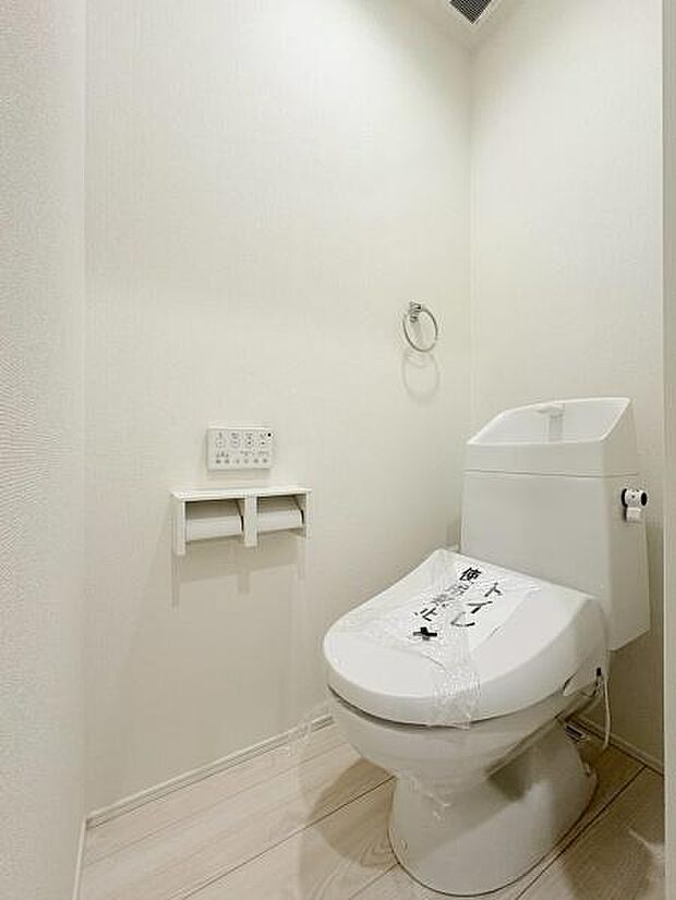 白を基調とした清潔感のあるトイレです。壁や床の色合いが統一されすっきりとした印象です。ペーパーホルダーや操作パネルも見やすく配置されています。収納や水回りもシンプルで使いやすい設備になっています。