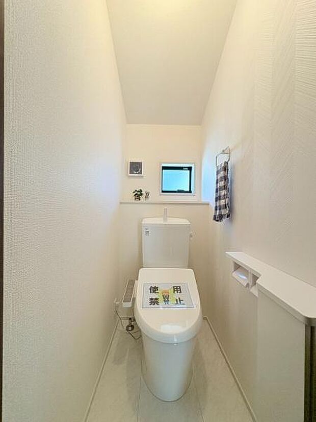 シンプルなデザインで清潔感のあるトイレです。小窓付きで換気もしっかりと行えます。タオル掛けやペーパーホルダーが配置されており使い勝手が考えられています。奥行きのある空間設計となっています。