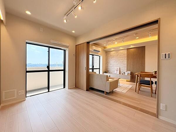 洋室は開放感のある空間が広がりバルコニーに面した大きな窓から自然光がしっかり差し込みます。床や壁は明るい色調で統一されています。リビングと洋室がスライドドアでつながっており、空間の使い分けが柔軟です。