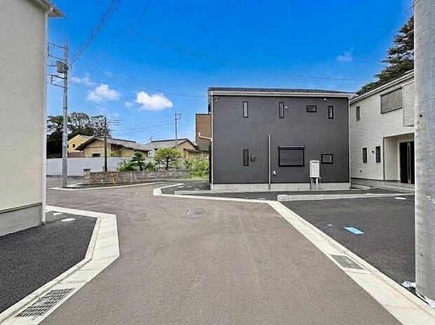 広々とした前面道路が印象的な現地写真です。周辺には新築住宅が並び落ち着いた雰囲気が感じられます。道路部分は舗装され住まいへのアクセスも安心です。電柱や街並みもすっきりとしており清潔感があります。