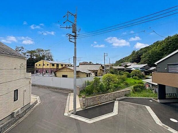 窓から広がる現地からの眺望は周囲の住宅や緑が調和した開放的な景色です。青空とともに見える住宅街の街並みが目を引きます。道路も広く周辺には植物の緑が広がっています。角地の位置も分かりやすい眺めです。