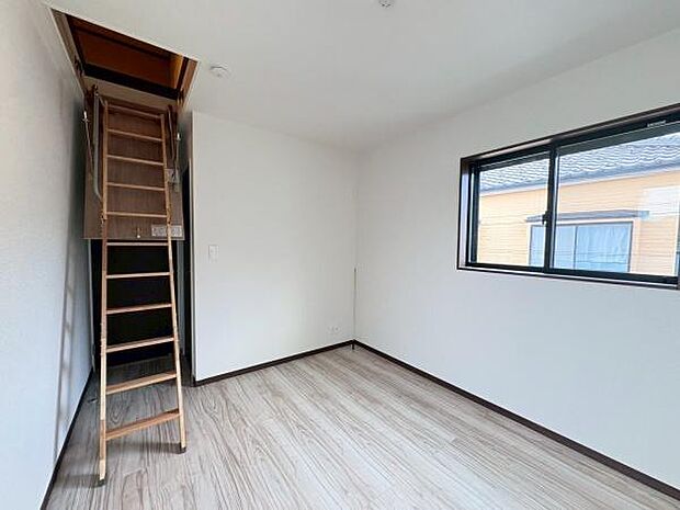 木目調のフローリングは、温かみと上質な雰囲気を演出。天井には小屋裏収納へと続く梯子があり、季節物の収納や趣味のスペースなど、空間を有効活用できます。