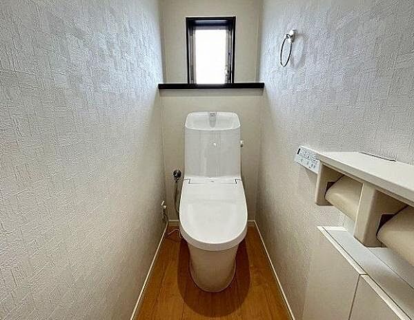 白を基調としたクロスと木目調フロアが調和した、明るく清潔感のあるトイレ空間です。壁掛けリモコンタイプの温水洗浄便座を装備。いつでも快適・衛生的にご利用いただけます。
