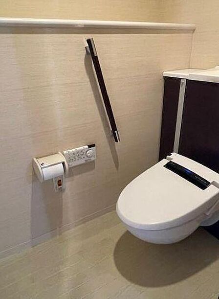 清潔感のある内装のトイレ、スマートな壁付けリモコンを採用しています。しっかりとした手すりが設置されており立ち座りの動作をさりげなくサポートしてくれます。