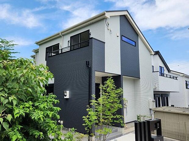 ホワイト×ダークグレーのスタイリッシュな外観が目を惹く住まい。アプローチの鮮やかなシンボルツリーと周囲の自然が美しく調和します。スタイリッシュなデザインと緑豊かな環境の両方を享受できます。