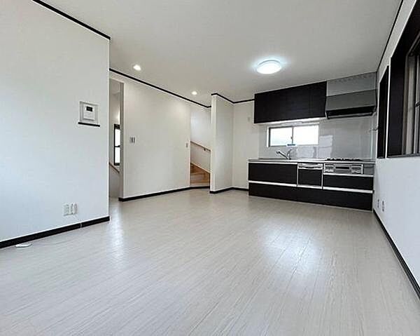 白を基調とした明るい内装に、ダークカラーの建具とシステムキッチンが引き締まる、洗練されたモダンスタイルのLDKです。フロアやクロスの清潔感とシックなアクセントが調和し、上質な空間を演出します。