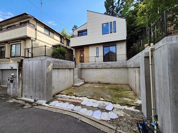 高台に佇む、白と木目のコントラストが美しいスタイリッシュな邸宅。道路から一段高い位置に建物を配置することで、通行人の視線を遮り、プライバシーと開放感を実現しています。