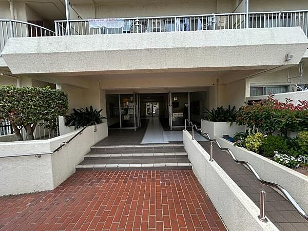 赤レンガ調のアプローチや綺麗に植栽された緑が、住まい手のこだわりや管理体制の良さを物語るエントランスです。スロープや手すりが設置されたバリアフリーに配慮した設計となっています。