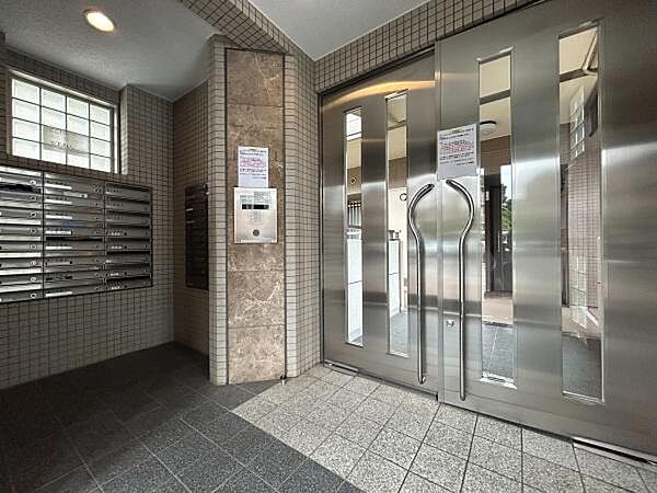 都会的なステンレス製のスタイリッシュなエントランスドアや、オートロック盤の背景にあしらわれたラグジュアリーな大理石調のアクセント壁が、建物全体の高い品格を表現しています。