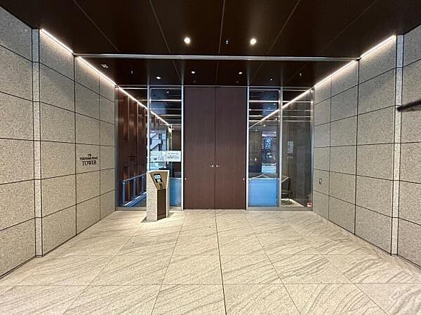 壁面の重厚な石材と、天井のダークトーン、そしてアクセントとなる木目調のドアが組み合わさり、ホテルライクな空間を演出。段差がなく、車椅子やベビーカー、大きな荷物を持った状態でもスムーズに移動できます。