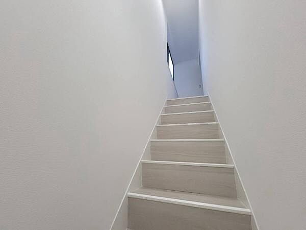 白を基調としたクロスと美しい木目調の踏み板が調和し、上階へと続く空間がとても爽やかで明るい雰囲気に仕上がっています。窓からの採光も感じられる心地よい設計です。