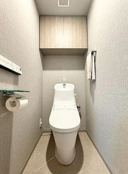 グレーを基調とした落ち着きのあるクロスや、高級感のあるフロアタイルを採用したスタイリッシュなトイレスペースです。上部にはトイレットペーパーや掃除用具などをすっきりと収納できる吊戸棚を完備しています。