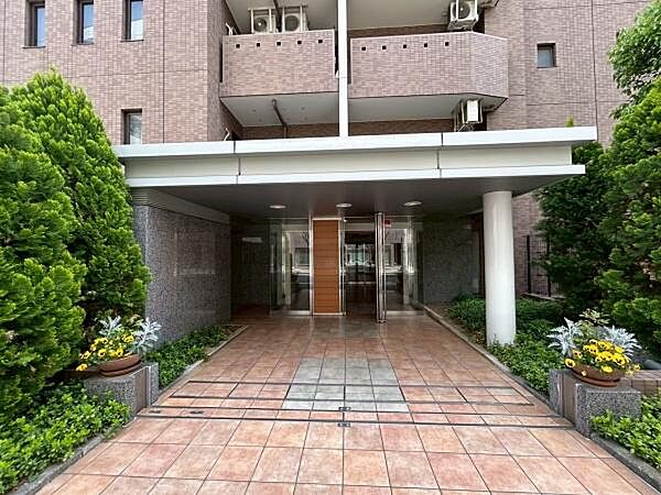 手入れの行き届いた鮮やかな植栽や季節の花々が、住まう方やゲストを温かくお迎えします。 温もりを感じさせる色合いのタイル敷きが、建物へと続くアプローチを上品に演出しています。