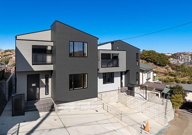 ゆとりあるカースペースと、日当たりの良い南面の庭を確保した配置計画。白とグレーを基調としたモダンな外観デザインが、青空に映える存在感のある住まいです。